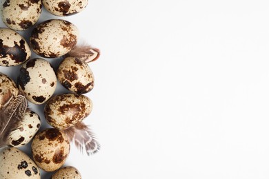 Photo of Speckled quail eggs and feathers on white background, flat lay. Space for text