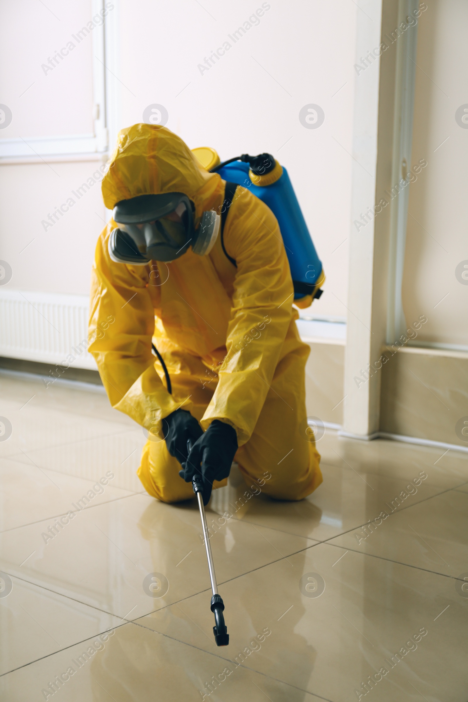 Photo of Pest control worker in protective suit spraying pesticide indoors