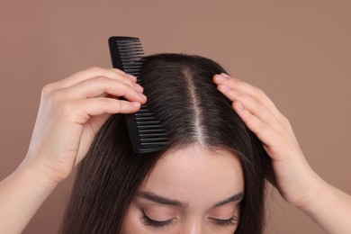 Photo of Woman with comb examining her hair and scalp on beige background, closeup