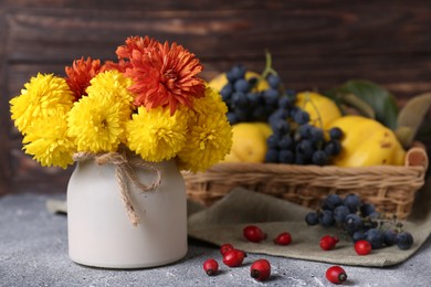 Bouquet of beautiful chrysanthemum flowers, rose hip berries and sweet fruits on grey table. Space for text