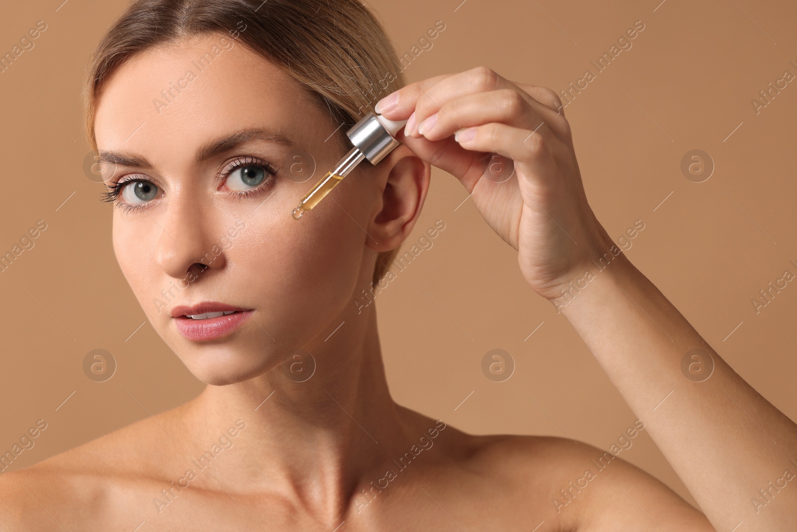 Photo of Beautiful woman applying cosmetic serum onto her face on beige background, closeup