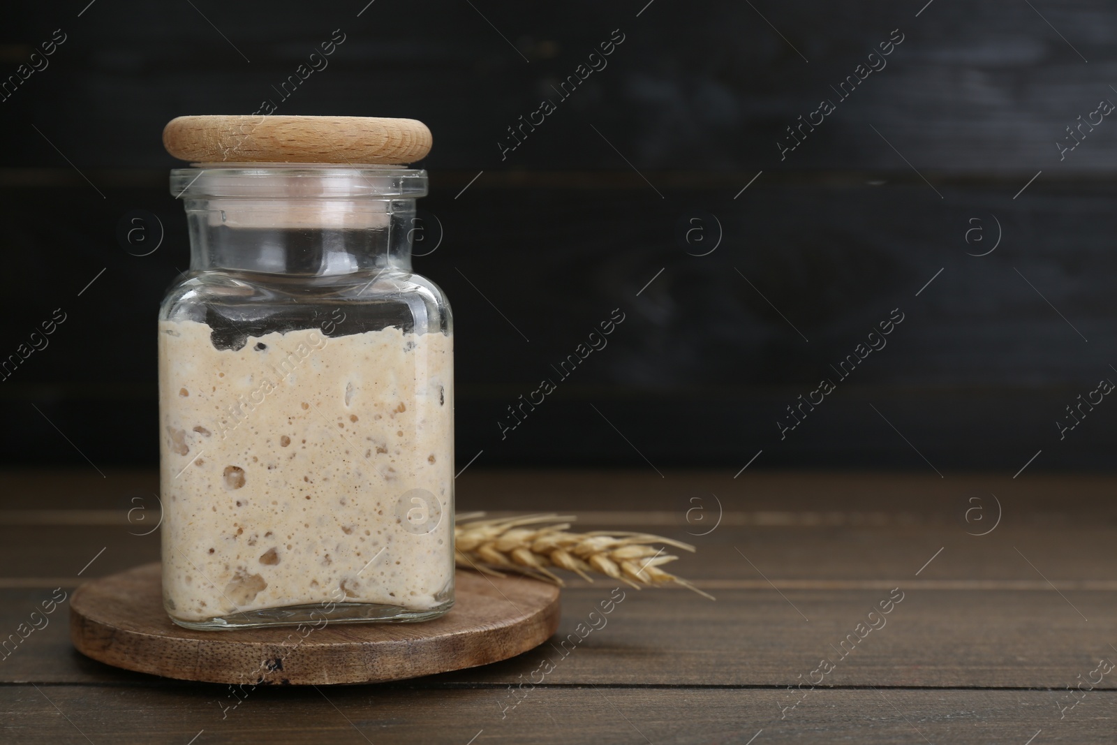 Photo of Leaven and ear of wheat on wooden table, space for text