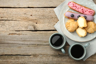 Aromatic coffee in cups, tasty eclairs and profiteroles on wooden table, top view. Space for text