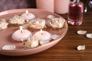 Photo of Bowl with water, burning candles and roses on wooden table, closeup. Space for text