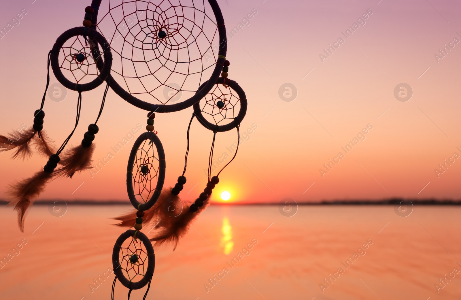 Photo of Beautiful handmade dream catcher near river at sunset. Space for text