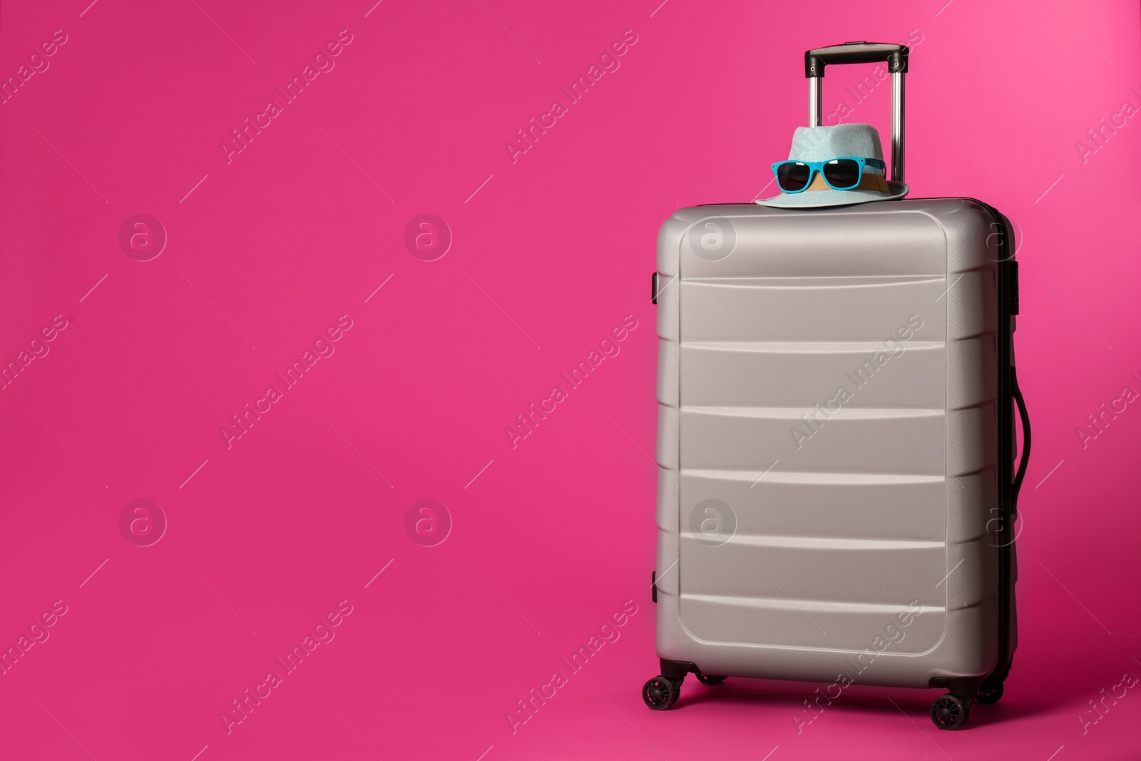 Photo of Stylish suitcase with hat and sunglasses on color background. Space for text