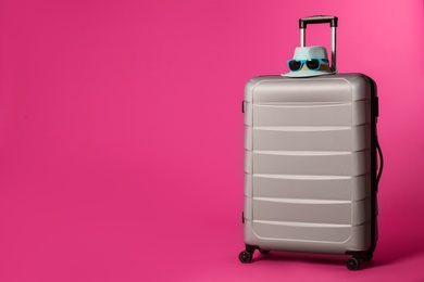 Stylish suitcase with hat and sunglasses on color background. Space for text