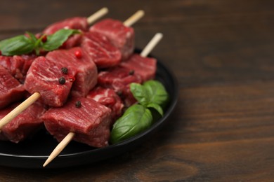 Photo of Skewers with cut fresh beef meat, basil leaves and spices on wooden table, closeup. Space for text