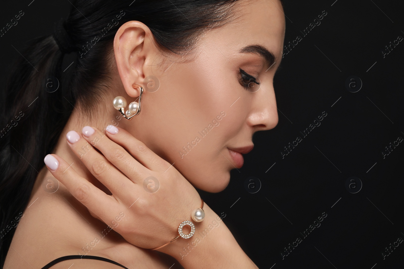 Photo of Young woman with elegant pearl jewelry on black background, closeup