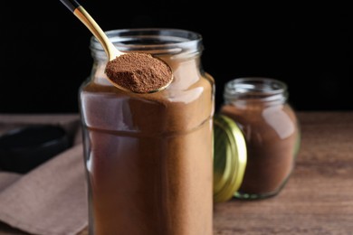 Photo of Spoon of instant coffee near jars on wooden table