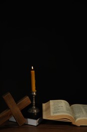 Photo of Church candle, Bible and cross on wooden table against black background