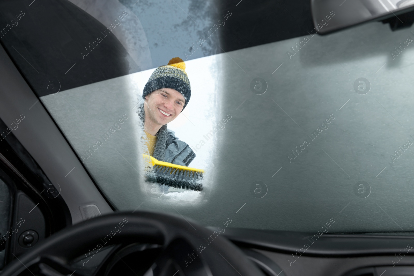 Photo of Man cleaning snow from car windshield, view from inside