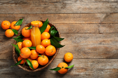 Basket with fresh tangerines and bottle of juice on wooden table, flat lay. Space for text