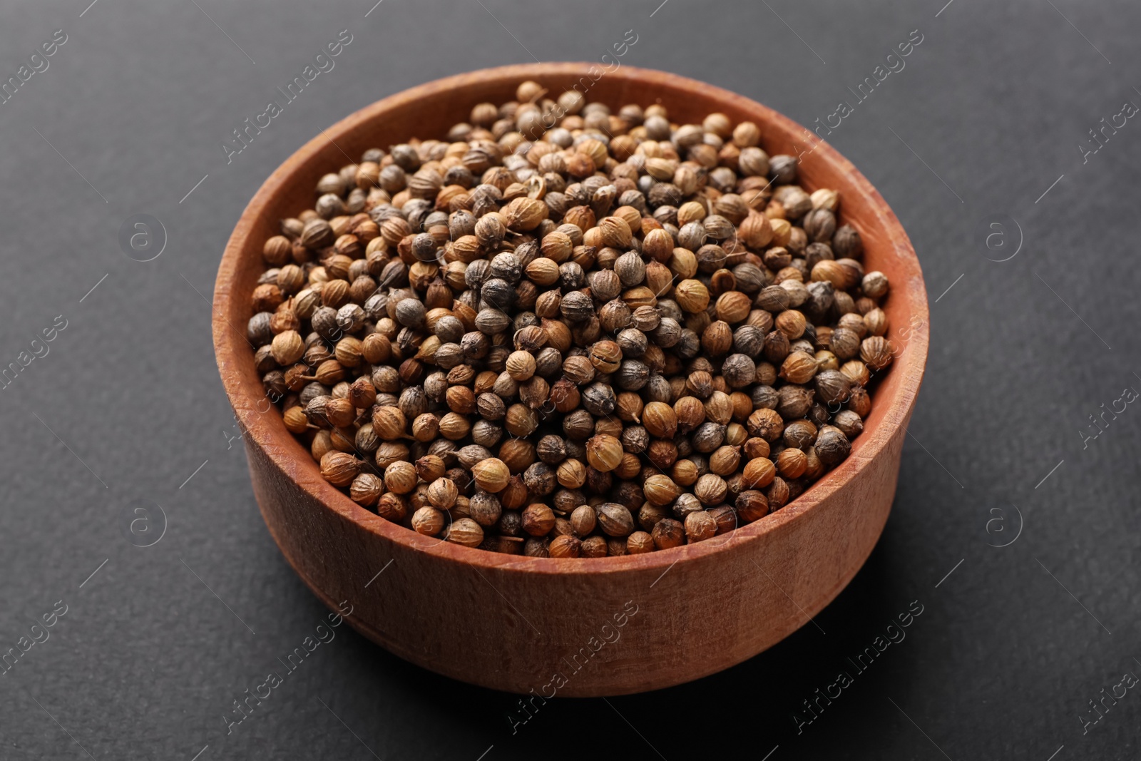 Photo of Wooden bowl of coriander grains on dark background