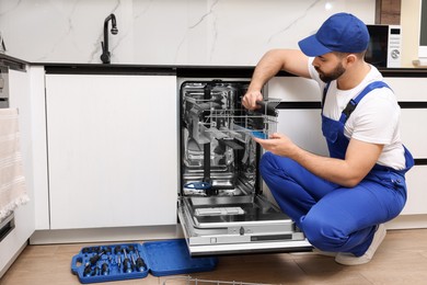 Photo of Serviceman repairing dishwasher cutlery rack in kitchen