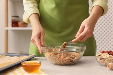 Photo of Woman making granola at light marble table in kitchen, closeup