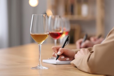 Photo of Sommeliers making notes during wine tasting at table indoors, closeup
