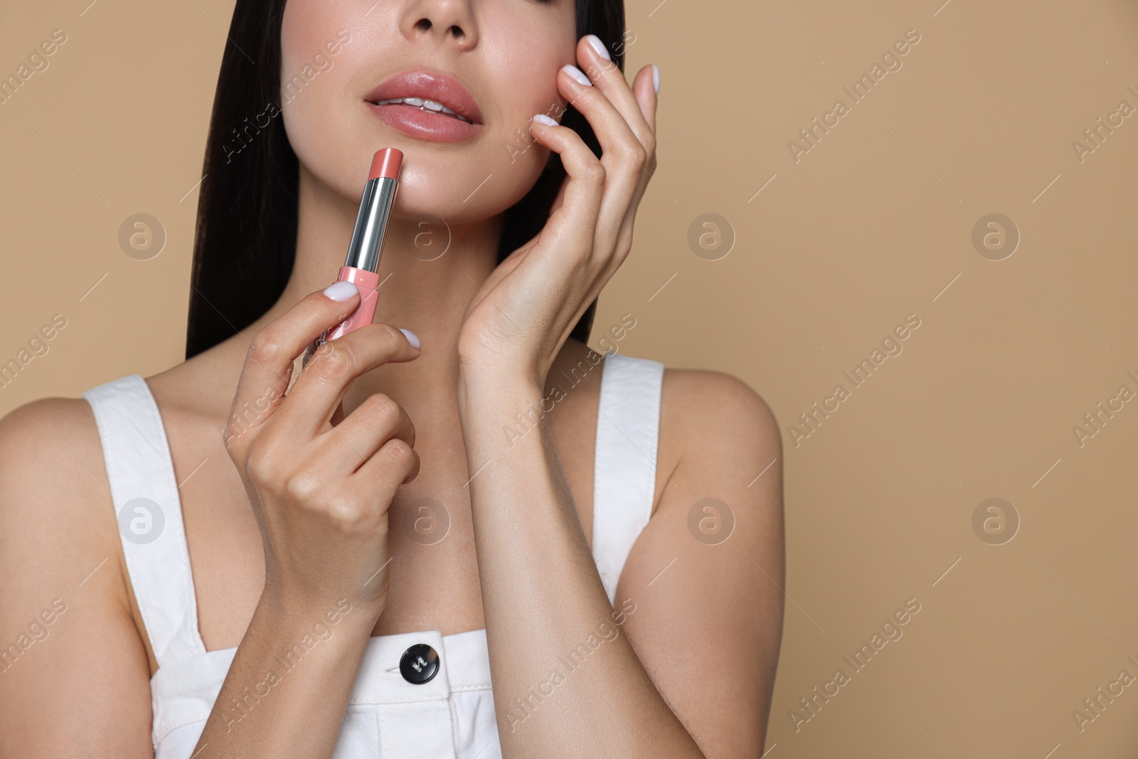 Photo of Young woman with beautiful makeup holding nude lipstick on beige background, closeup. Space for text