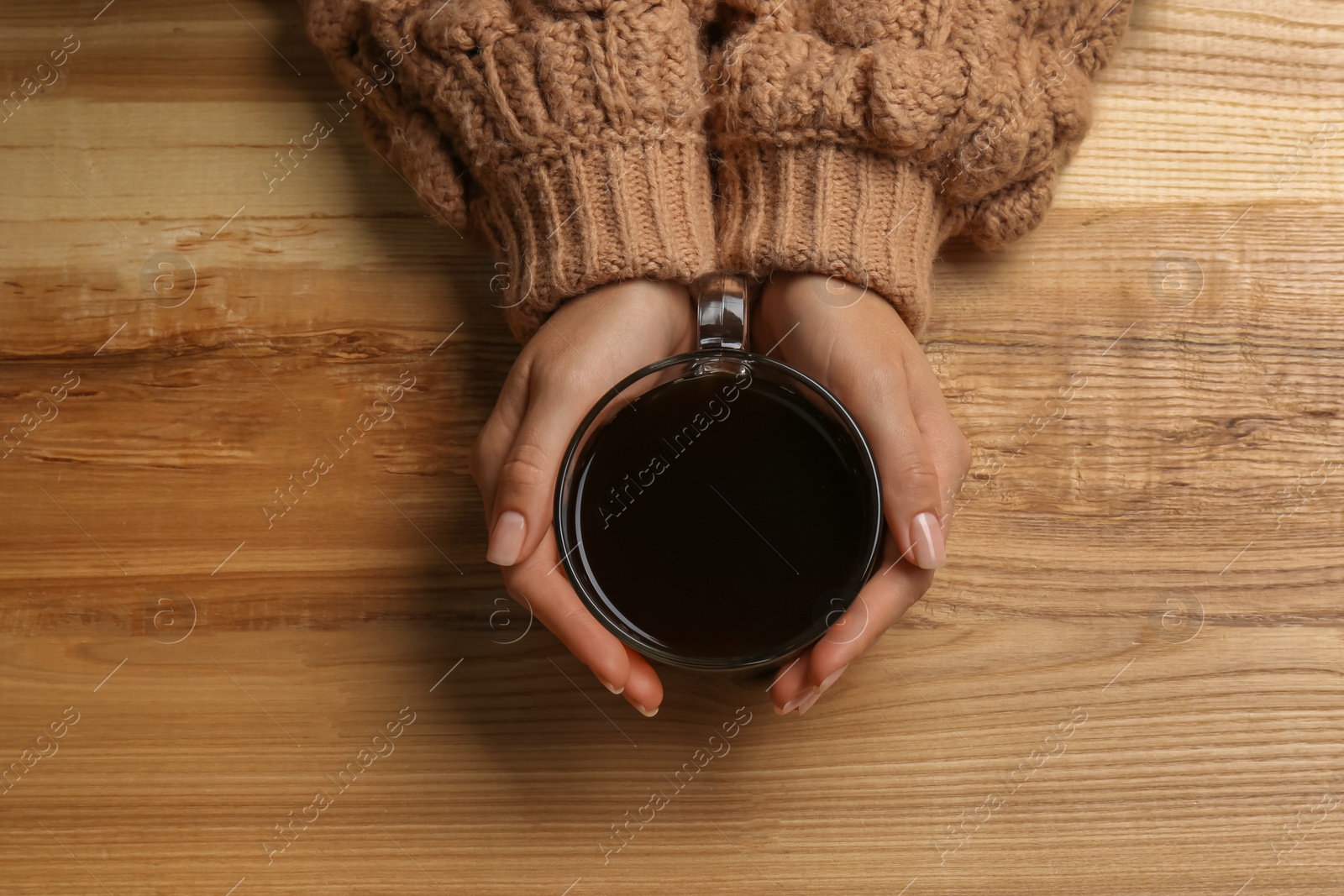 Photo of Woman holding glass cup of tea at wooden table, top view