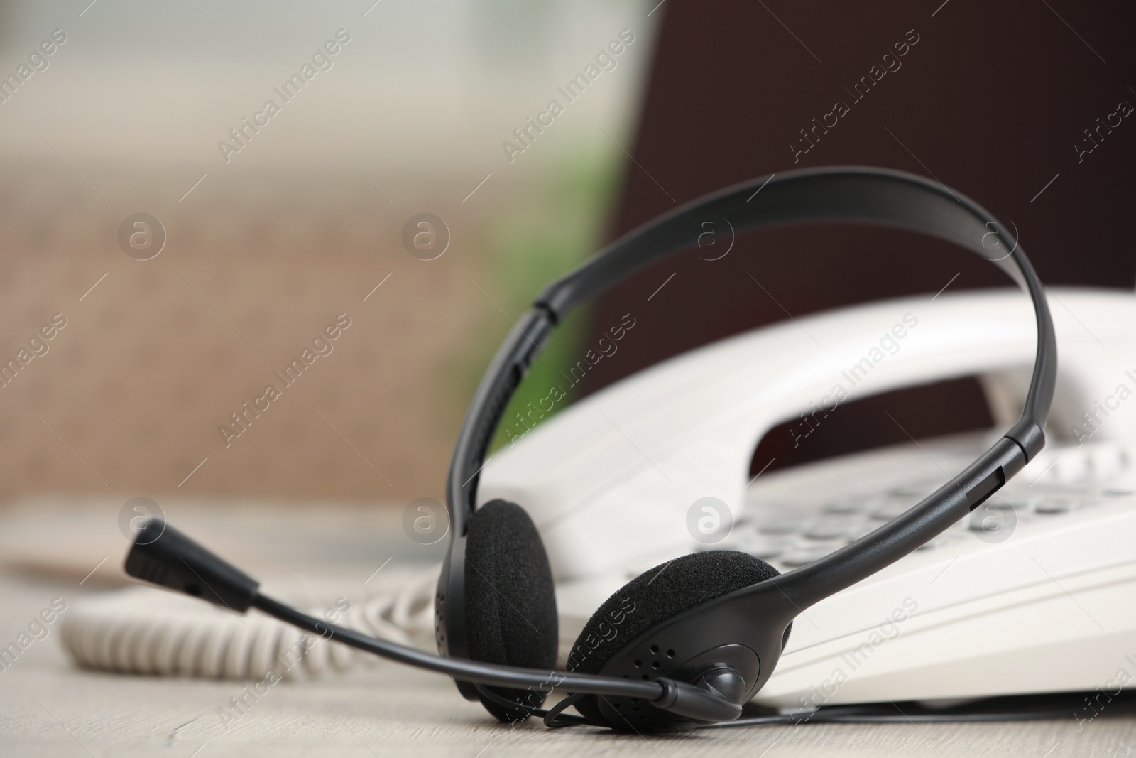 Photo of Headset and desktop telephone on table indoors, closeup. Hotline concept