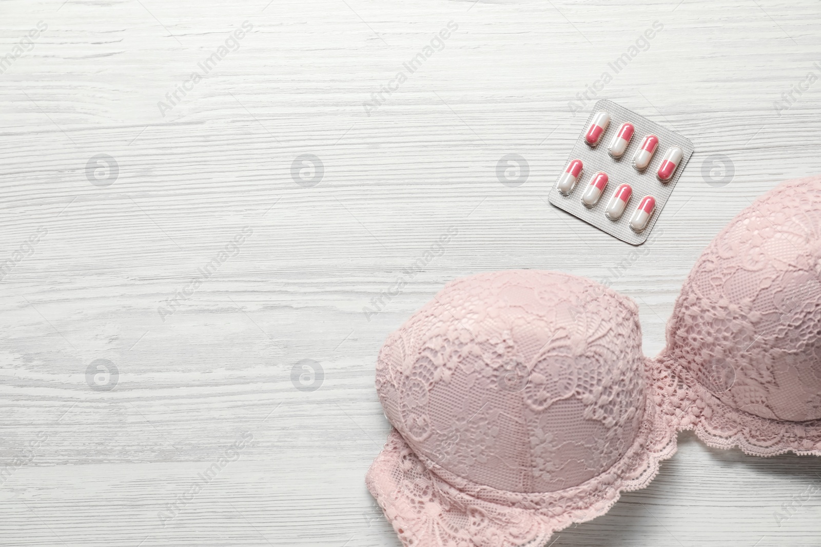 Photo of Breast cancer awareness. Bra and pills on white wooden table, flat lay. Space for text