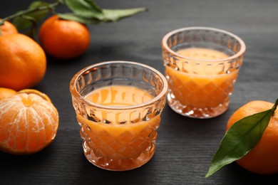 Photo of Tasty tangerine liqueur in glasses and fresh fruits on black wooden table