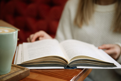 Woman reading book at table indoors, closeup