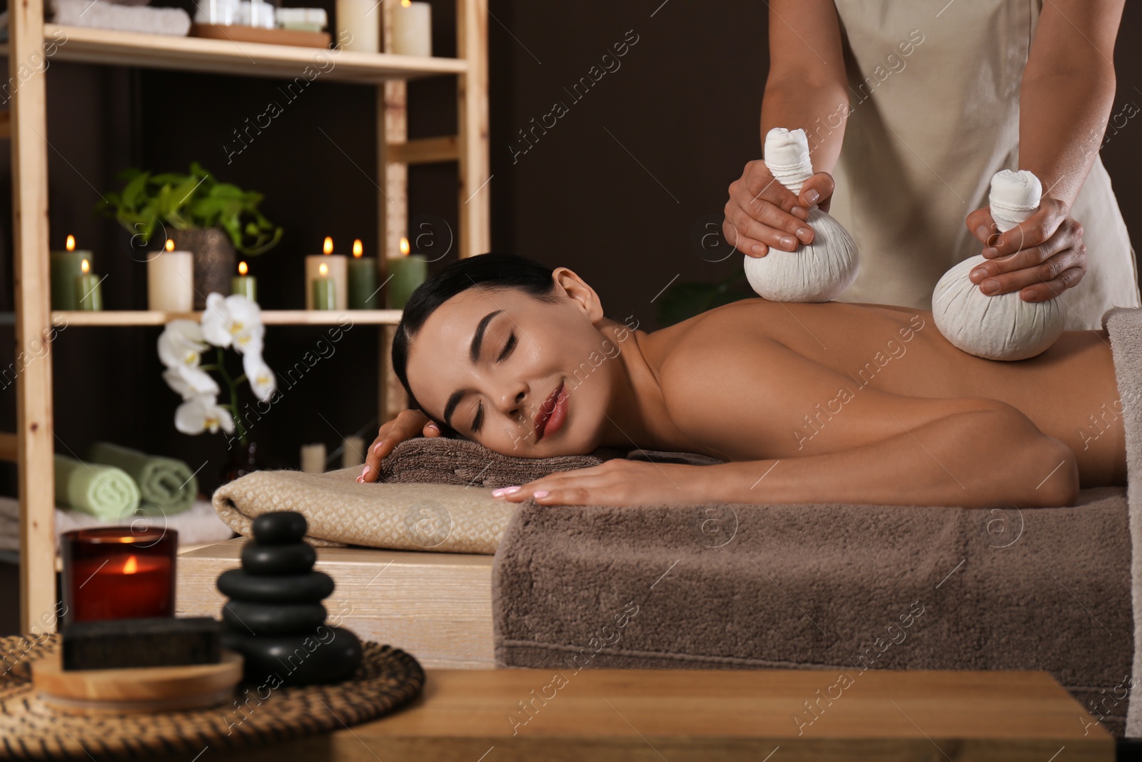 Photo of Young woman receiving herbal bag massage in spa salon