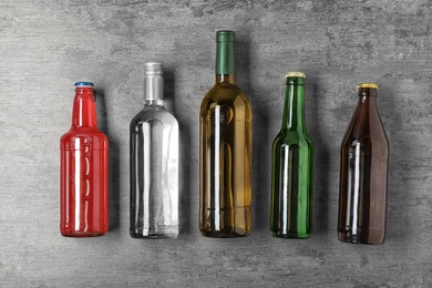 Bottles with different alcoholic drinks on grey background, top view