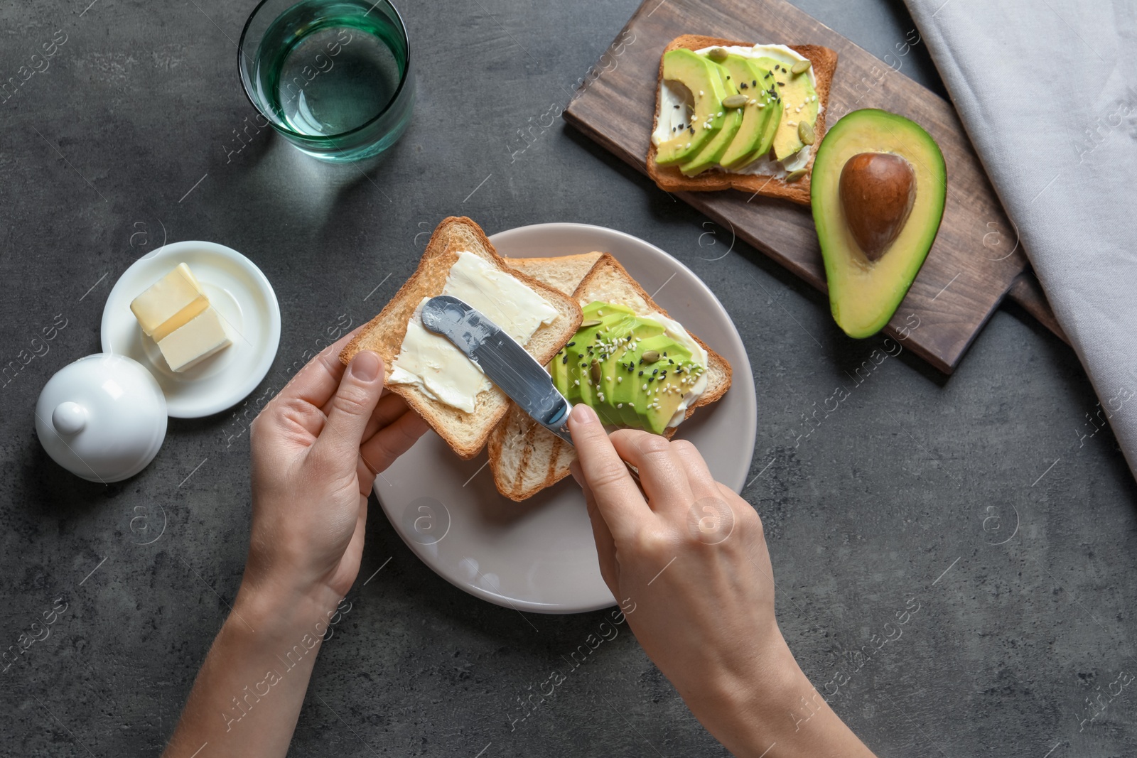 Photo of Woman spreading butter on toasted bread at table, top view