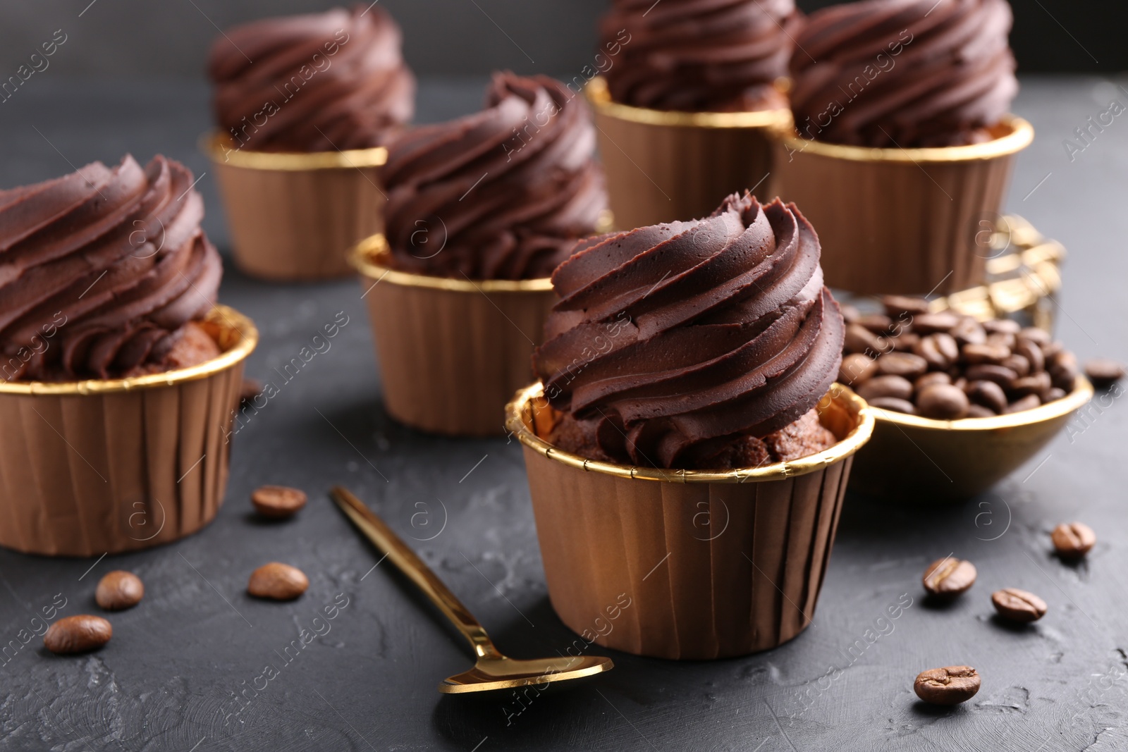 Photo of Delicious chocolate cupcakes and coffee beans on black textured table, closeup
