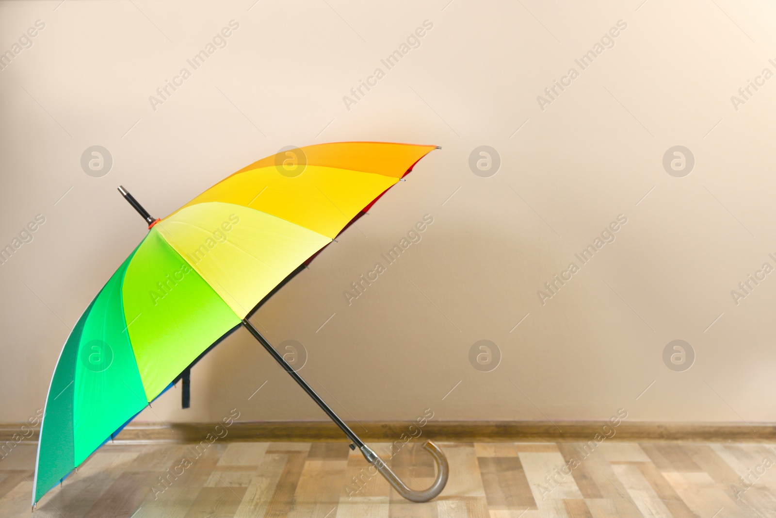 Photo of Beautiful open colorful umbrella near beige wall. Space for text