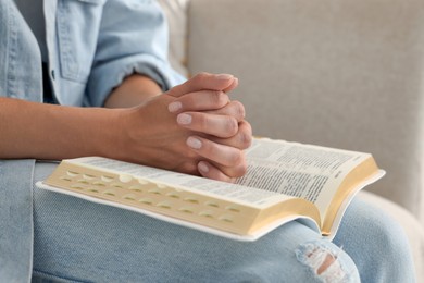 Religious woman with Bible praying indoors, closeup