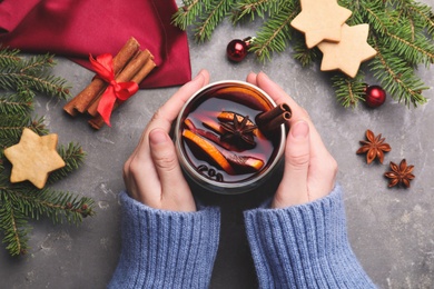Photo of Woman with glass of aromatic mulled wine at grey table, closeup