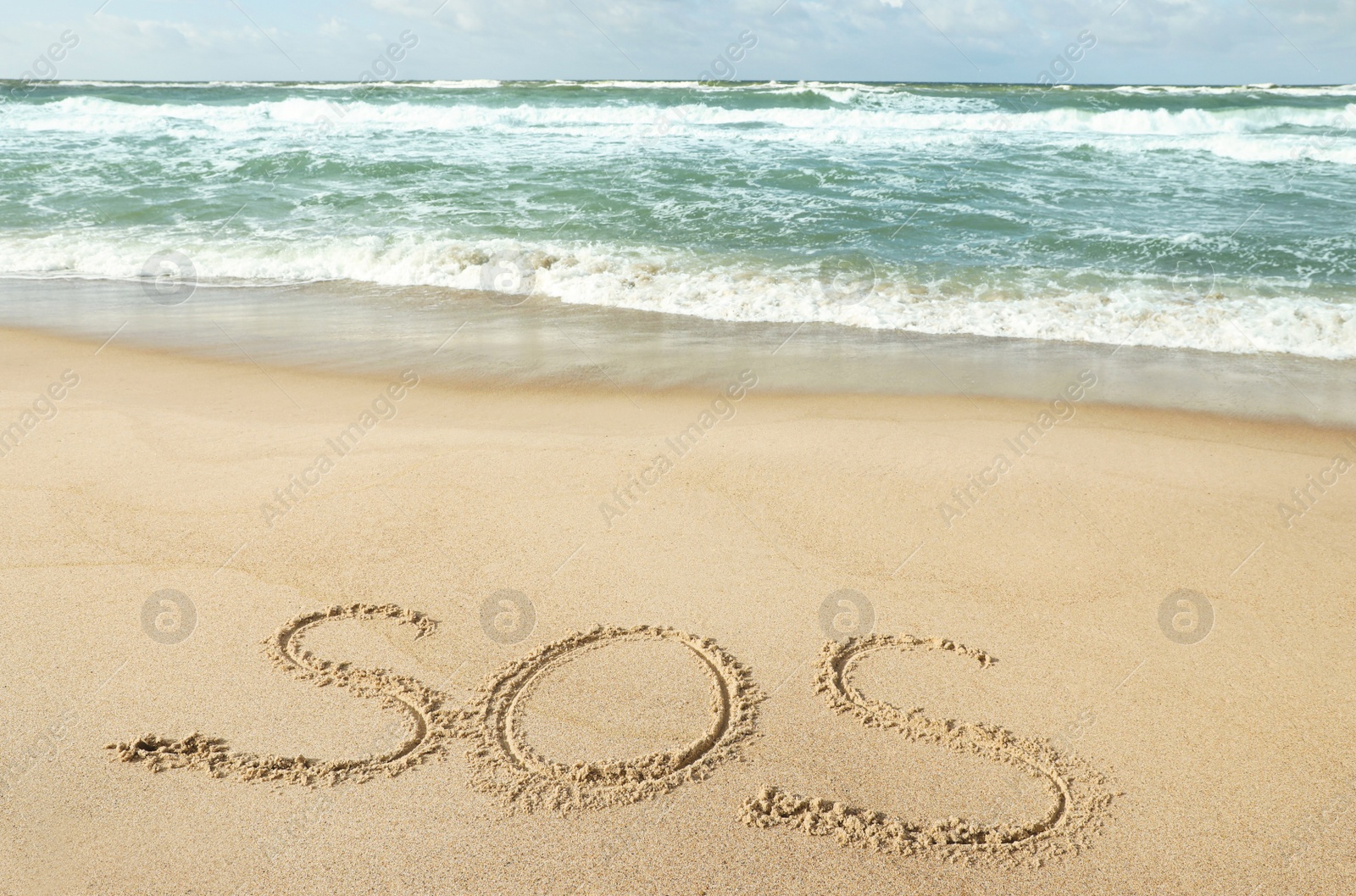 Photo of Message SOS drawn on sand near wavy sea