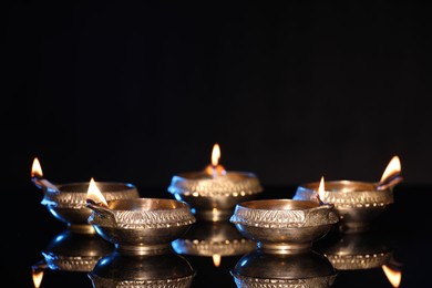 Many lit diyas on black background, space for text. Diwali lamps