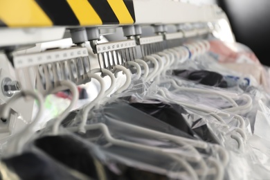 Photo of Hangers with clothes on garment conveyor at dry-cleaner's, closeup