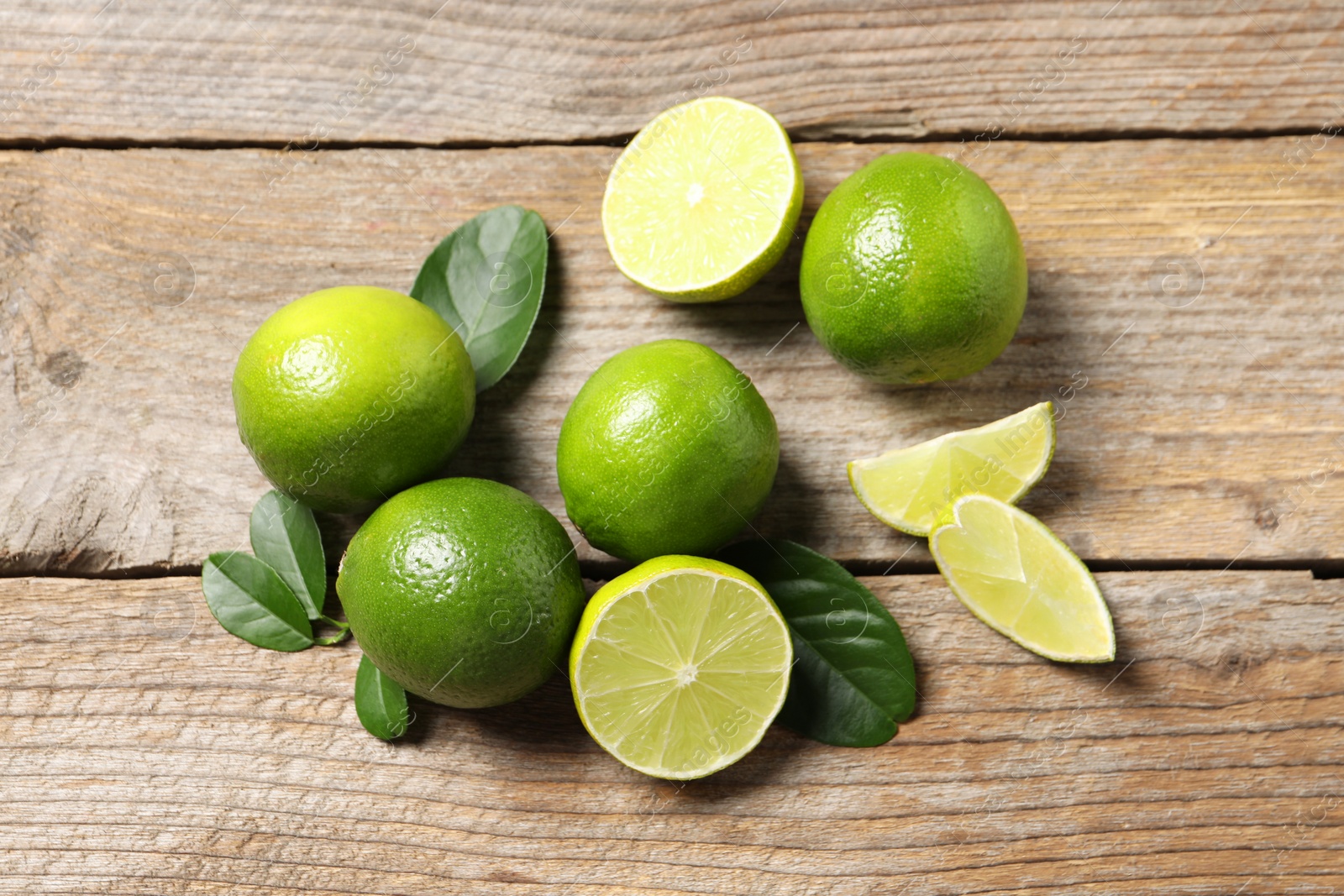 Photo of Fresh limes and green leaves on wooden table, flat lay