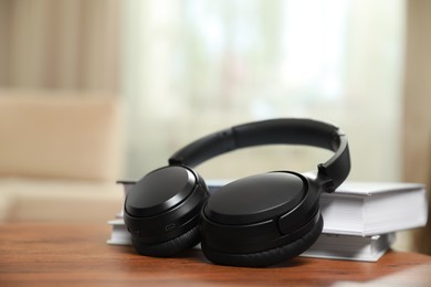 Photo of Modern wireless headphones and books on wooden table indoors, closeup