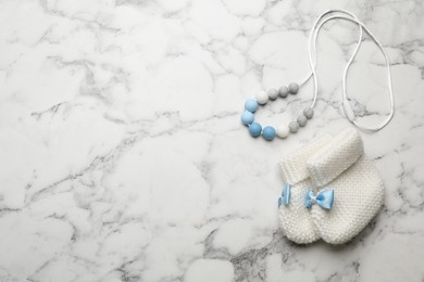 Photo of Cute baby booties and toy on white marble background, flat lay. Space for text