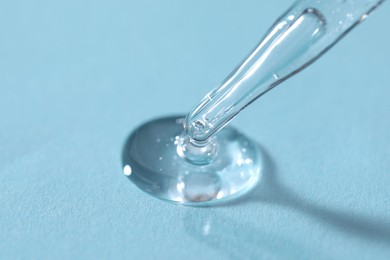 Glass pipette and transparent liquid on light blue background, closeup