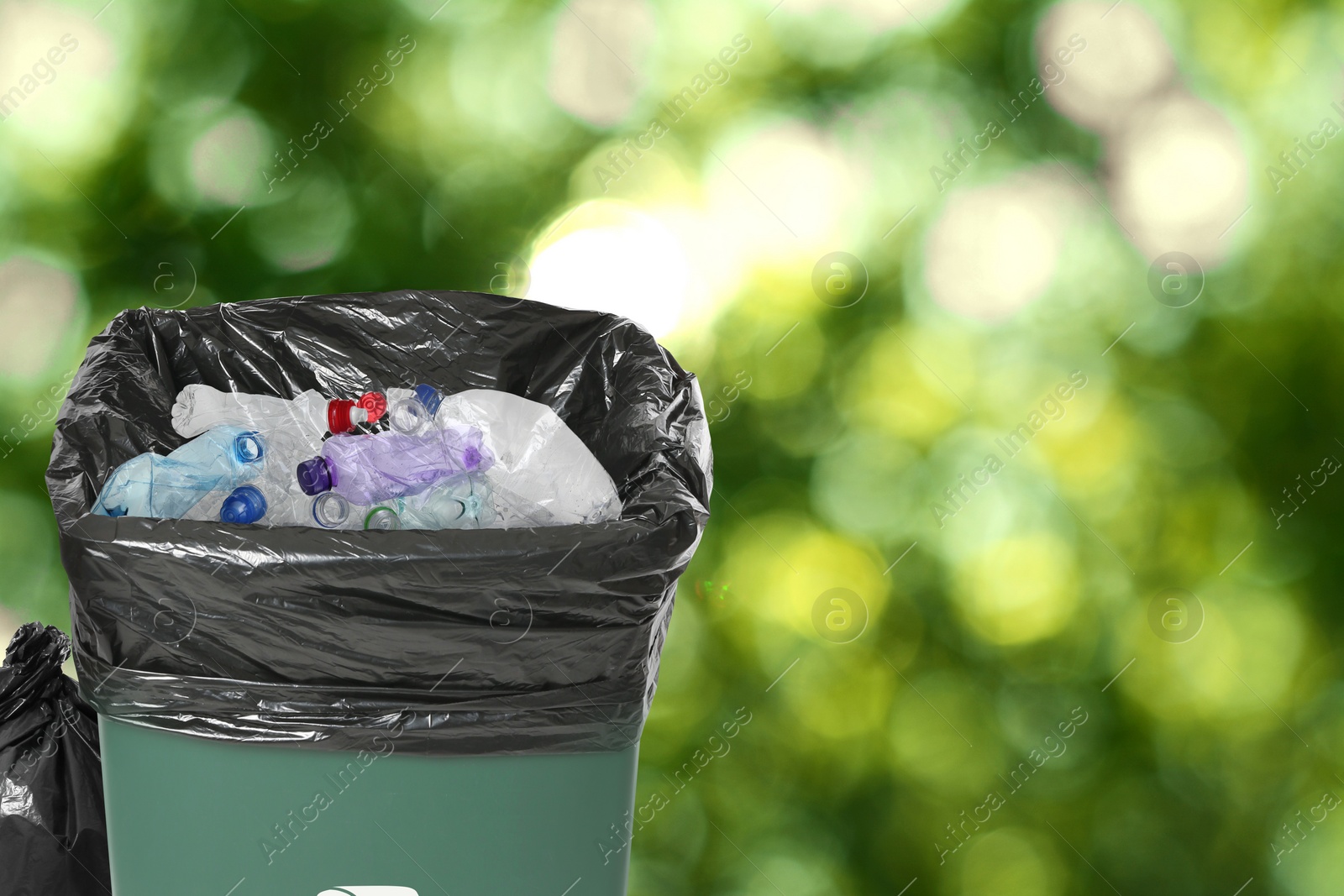 Image of Waste bin with plastic bag full of garbage on blurred background, space for text