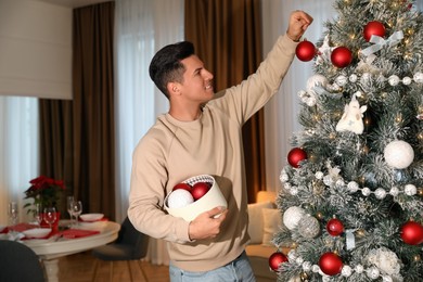 Photo of Handsome man decorating Christmas tree at home