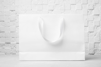 Photo of Paper shopping bag with ribbon handles on table near white wall. Mockup for design