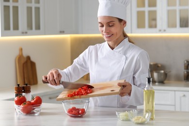 Photo of Professional chef putting cut tomatoes into bowl at white marble table indoors
