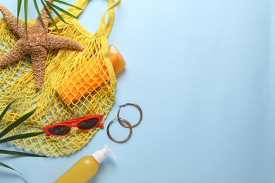 String bag, different beach accessories and palm leaves on light blue background, flat lay. Space for text