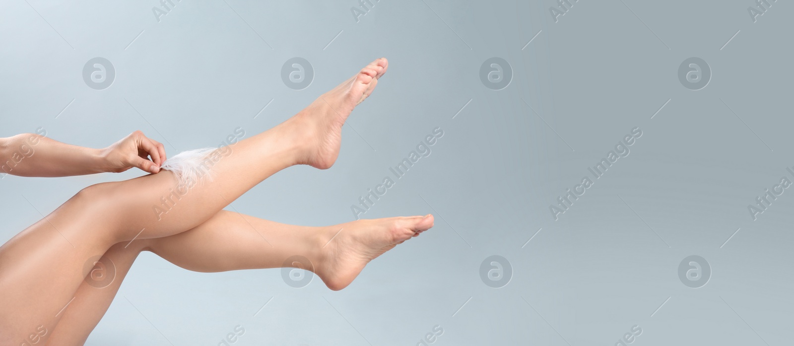 Image of Woman touching leg with feather after epilation on grey background, closeup view with space for text. Banner design