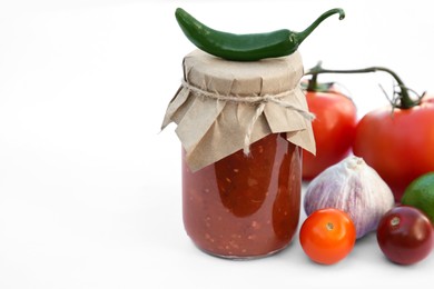 Jar with delicious salsa sauce and ingredients on white background, closeup. Space for text