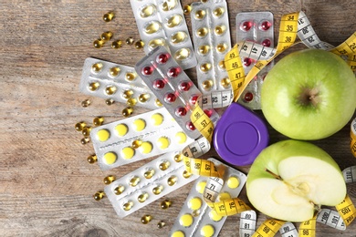 Photo of Weight loss pills with apples and measuring tape on wooden background, top view