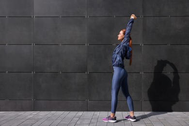 Beautiful woman in gym clothes doing exercises on street, space for text